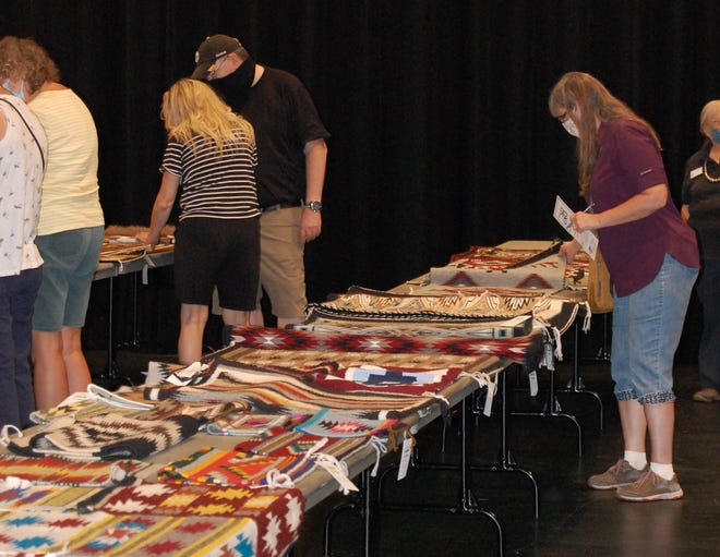 Potential bidders examine the items included in the Navajo Rug Auction at the 2021 Totah Festival & Indian Market at the Farmington Civic Center.