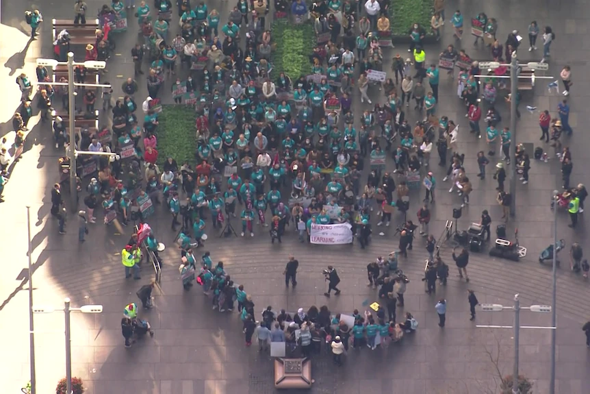 Hundreds of people wearing light green shirts and holding signs gather in the city of Sydney.