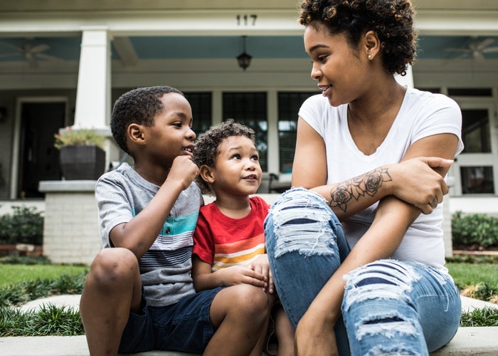 A mother talking with her two young sons while sitting in front of a house